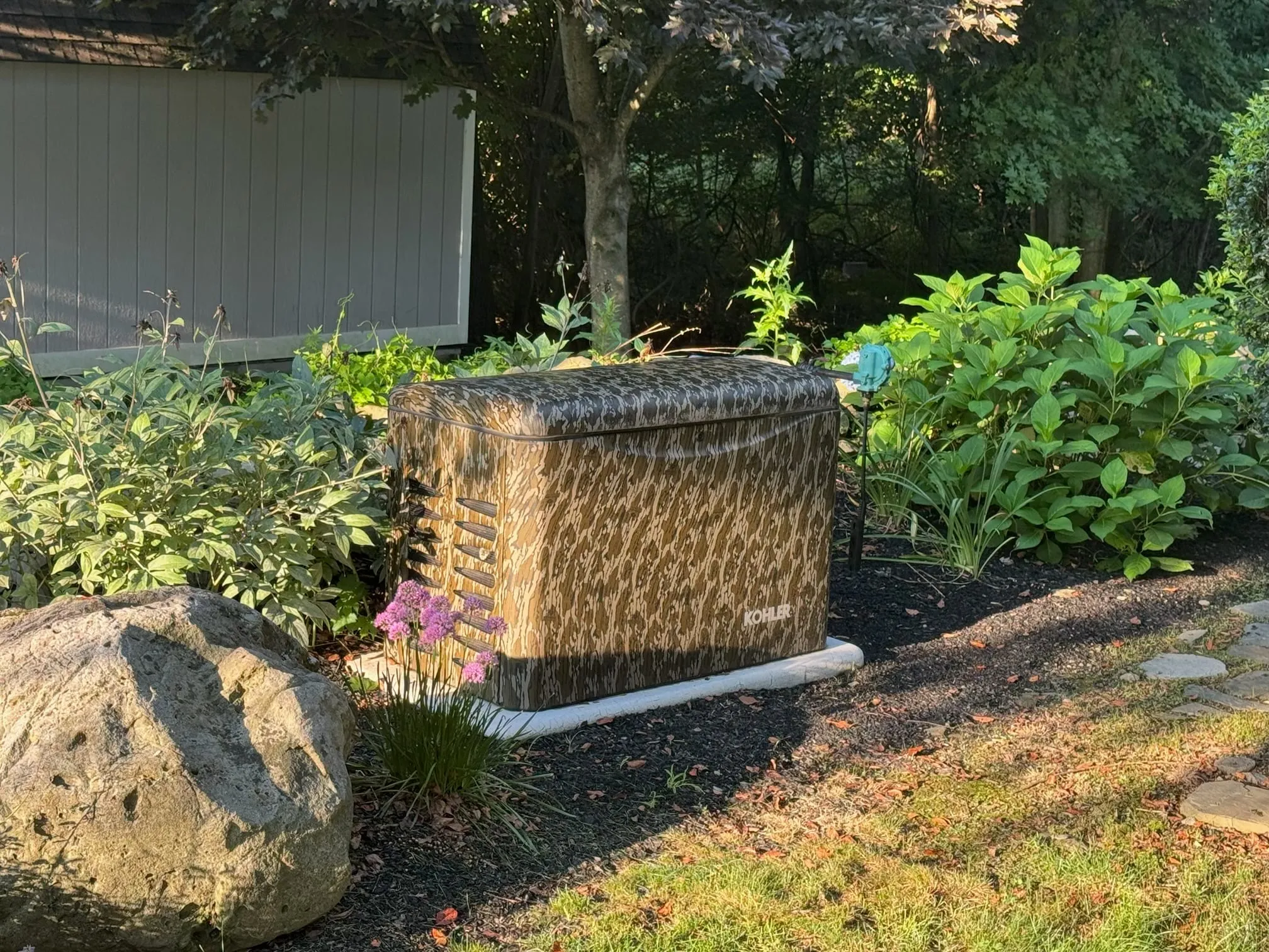 Kohler home standby generator in a camouflage finish, installed in a garden bed